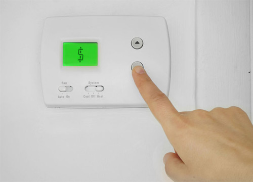 A dollar sign is displayed on the LCD display of a thermostat. A model's hand is pressing the thermostat's down button.